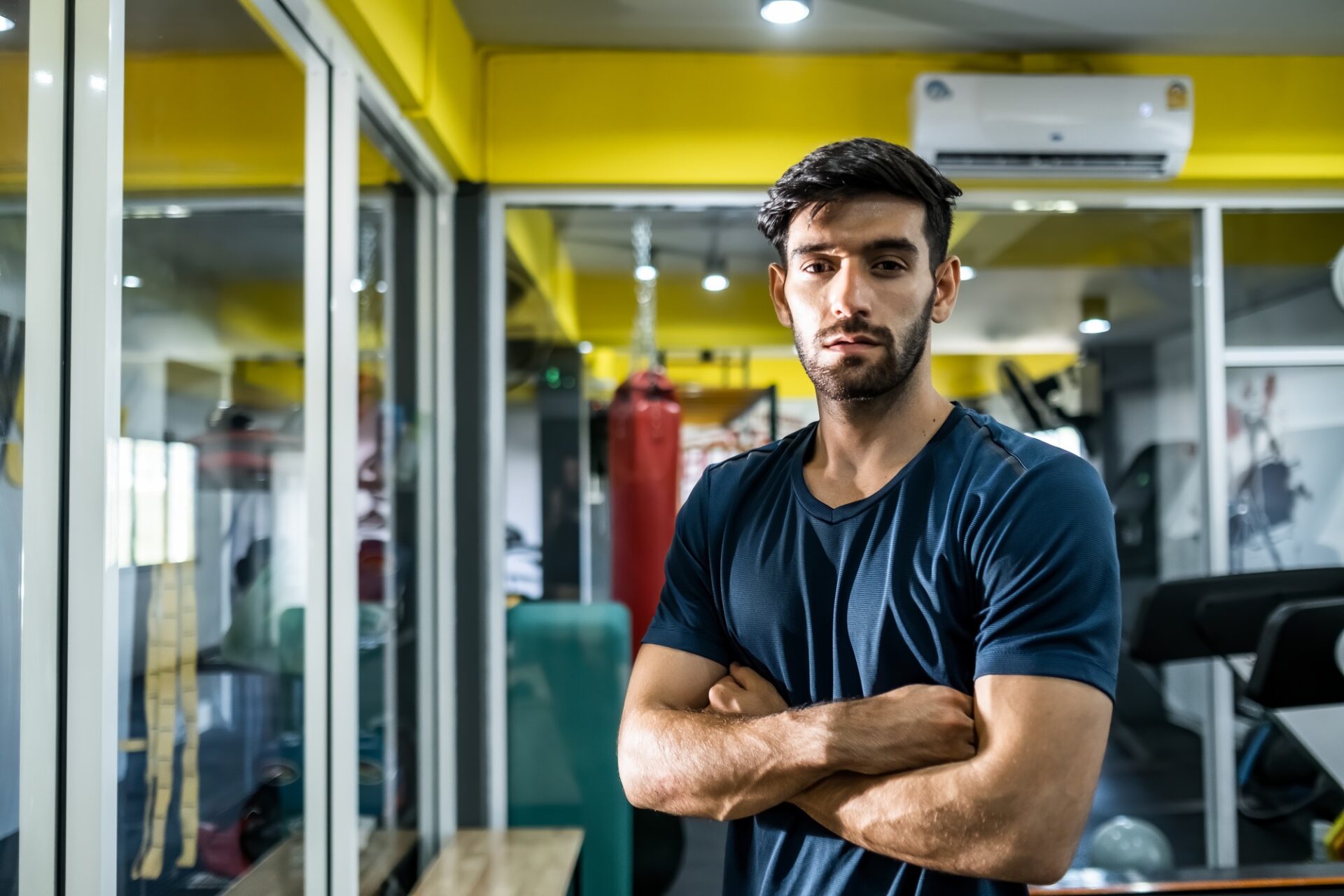 Portrait of young Caucasian man standing and putting hands on waist in gym or fitness club.